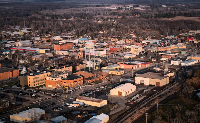 Aerial photo of downtown Aitkin, MN. We see the water town and lots of 1-3 story buildings. In the background, we can faintly make out the Aitkin airport. 
