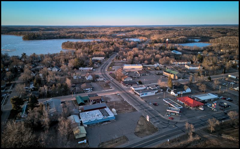 Aerial view of mainstreet in a small town. Scattered commercial businesses, surrounded by homes. There is a lake in the background.
