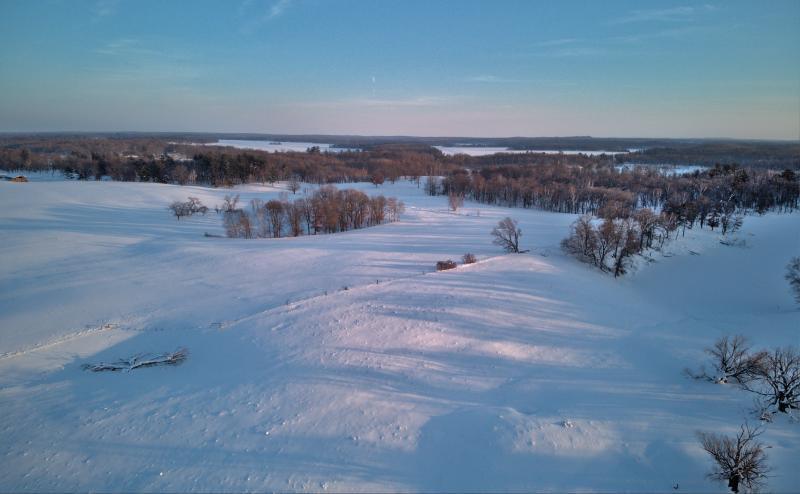 Photo of snow covered fields with patches of trees and frozen lakes in the distance.