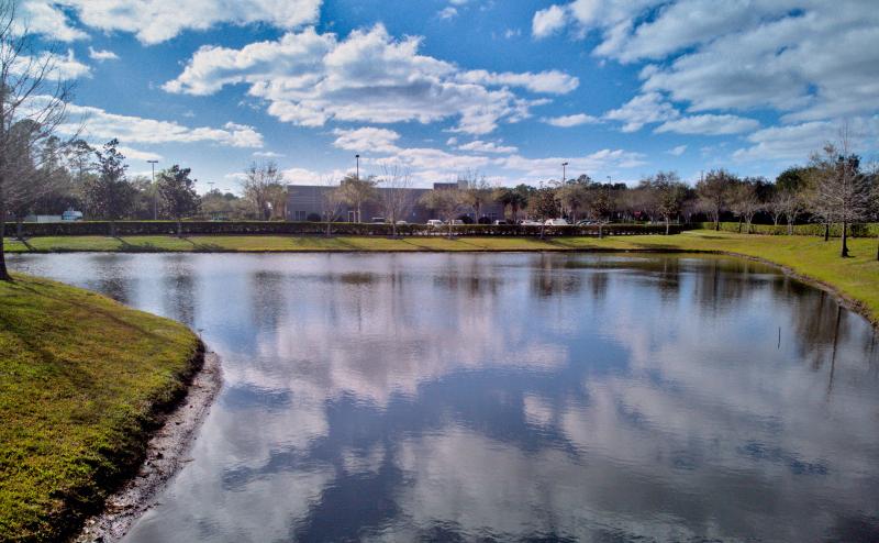 Blue sky and puffy white clounds reflect off the surface of a small pond in Orlando, Florida. 