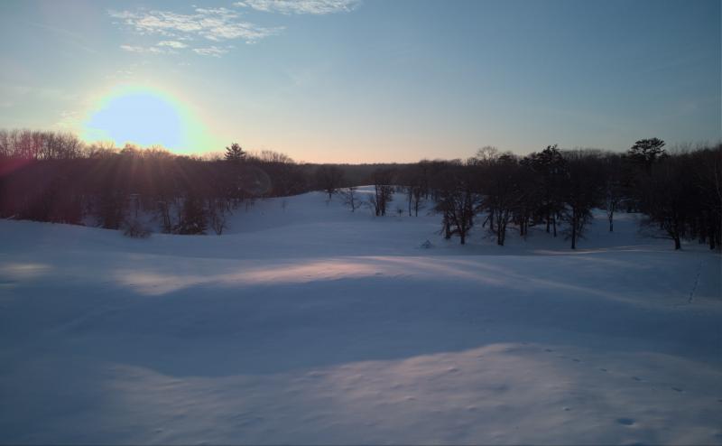 Rolling fields at sunset, casts long shadows over snow covered fields. Wisps of clouds in otherwise clear sky.