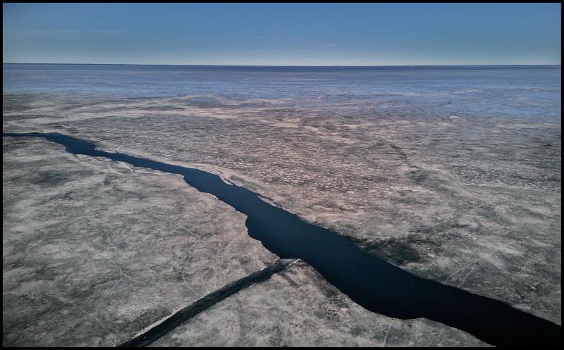 Aerial view of a large a place where two large cracks in the ice are coming together on a very large frozen body of water. We can not see shore in any direction. 