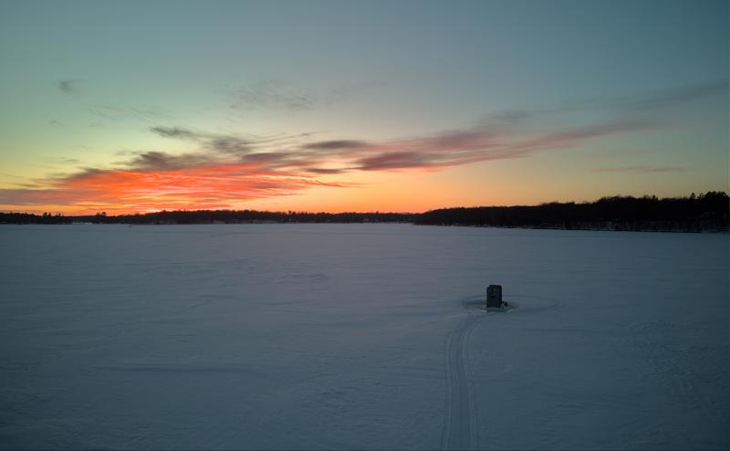 An orange sunset over a frozen lake with a solitary sunset in foreground