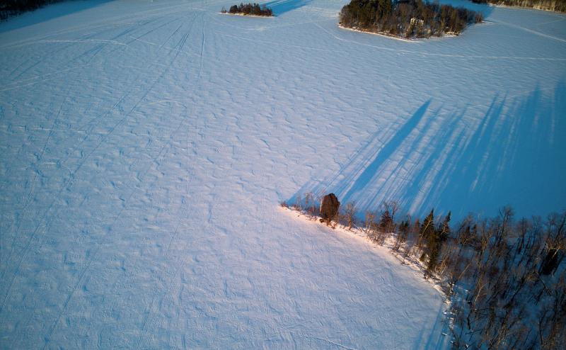 A pointy peninsula in a frozen and snow covered lake casts long shadows.