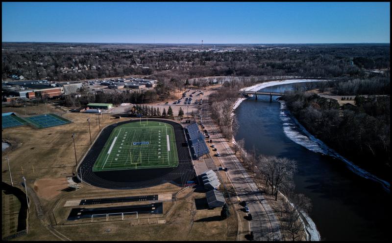 Aerial view of a football field alongside a river. The river has some ice along the edges.
