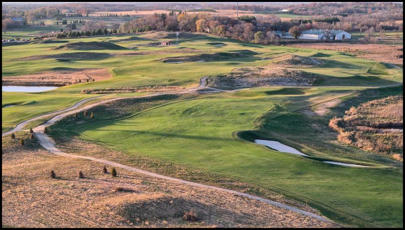 Aerial view (at an angle) of a bright green golf fairways without any vegitation between them or anyone playing gold. Bumps and mounds on fairways cast long shadows as it is clearly close to sundown.