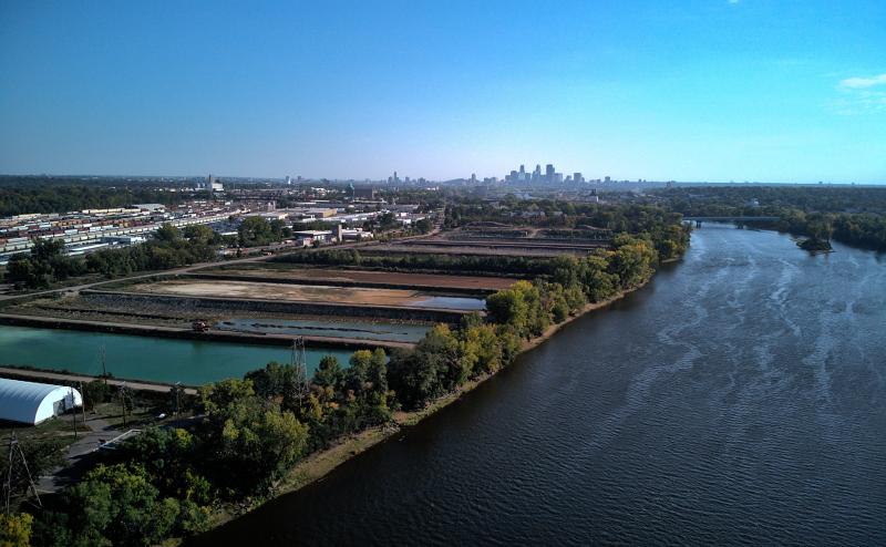 Aerial photograph looking south at downtown Minneapolis from just over the Mississippi. Rail yards to the left.