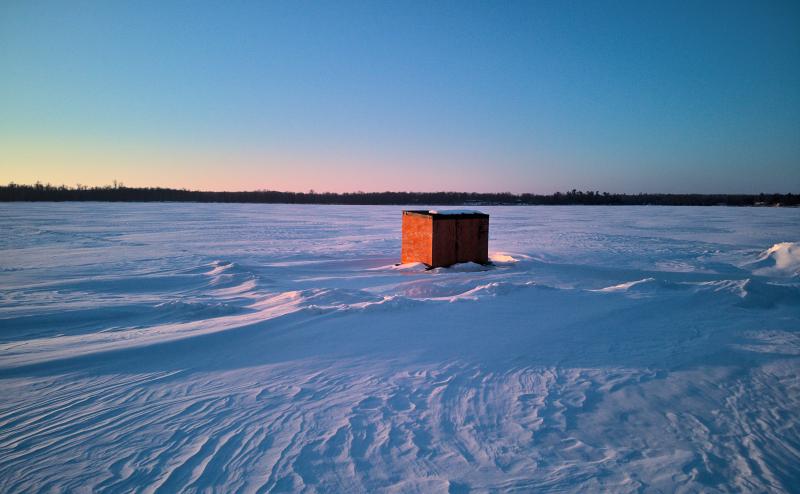 An orange ice house of a snow covered lake.