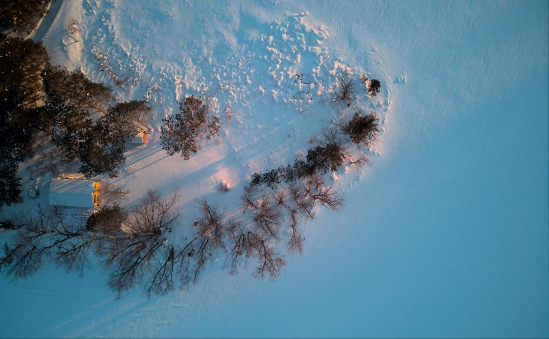 Looking down at a cabin on a peninsula that juts out into a frozen lake. 