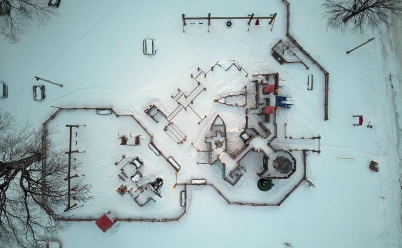 Looking straight down on a childrens playground in a local park. The ground is covered in snow and you can see the outline of each piece of playground.