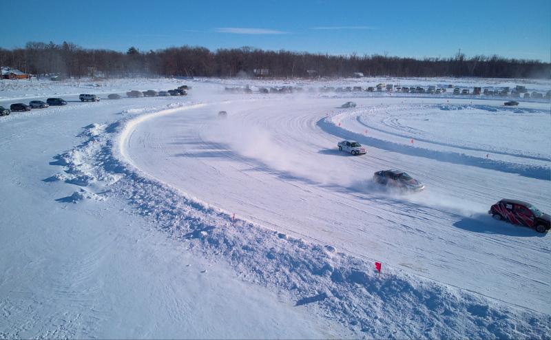 About 5 cars racing on an ice track on a frozen lake. 