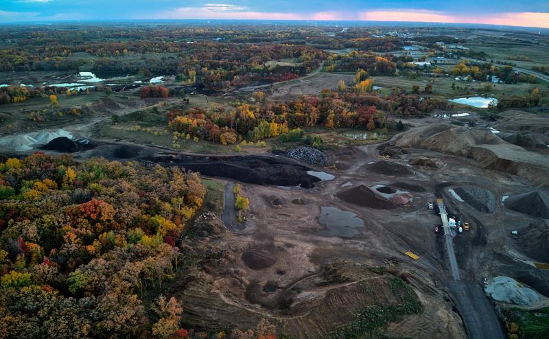 Aerial view of some kind of quarry with some heavy equipment and lots of piles of dirt/gravel of different colors (shades of grey or black).