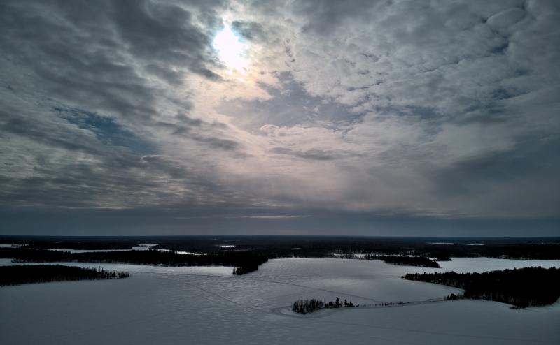 Looking down on snow and ice covered lake. Sun breaking through the clouds reflects off the snow on the lake.