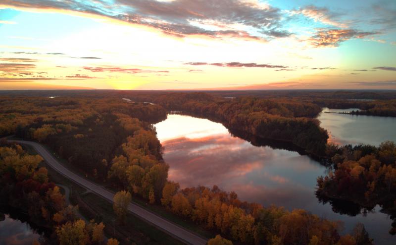 It's sunset over a forest of autumn colored trees and several clear lakes reflecting clouds in the sky. 