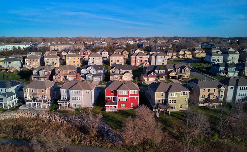 Rows of suburban houses without any mature trees. All the houses are very pale colors - except one house that is red and is in the middle of the first row.