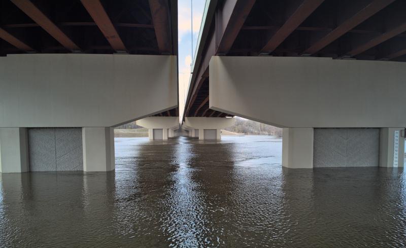 Underneath relatively new freeway bridge with high water. Looking straight across the river at the support structures. 